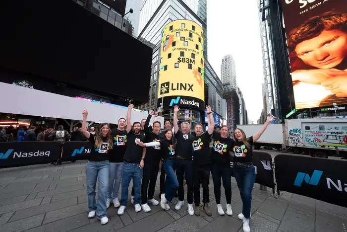 A group of ten people in black shirts celebrating in Times Square, beneath a large Nasdaq billboard displaying “Linx” and "$83M," conveying success and excitement.