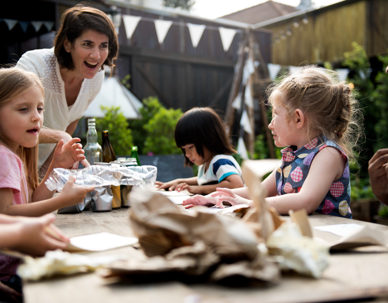 Group of children sitting around a table stacking colorful wooden blocks while an adult supervises.