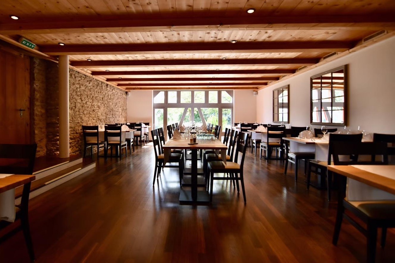 Restaurant mit Holzboden, Holzbalkendecke, Steinwand und gedeckten Tischen mit Stühlen.