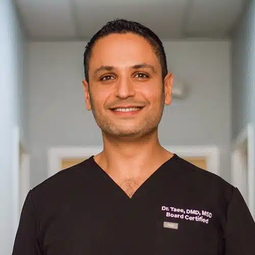 Smiling male healthcare professional wearing black scrubs with 'Dr. Taee, DMD, MSD Board Certified' embroidered on the chest.