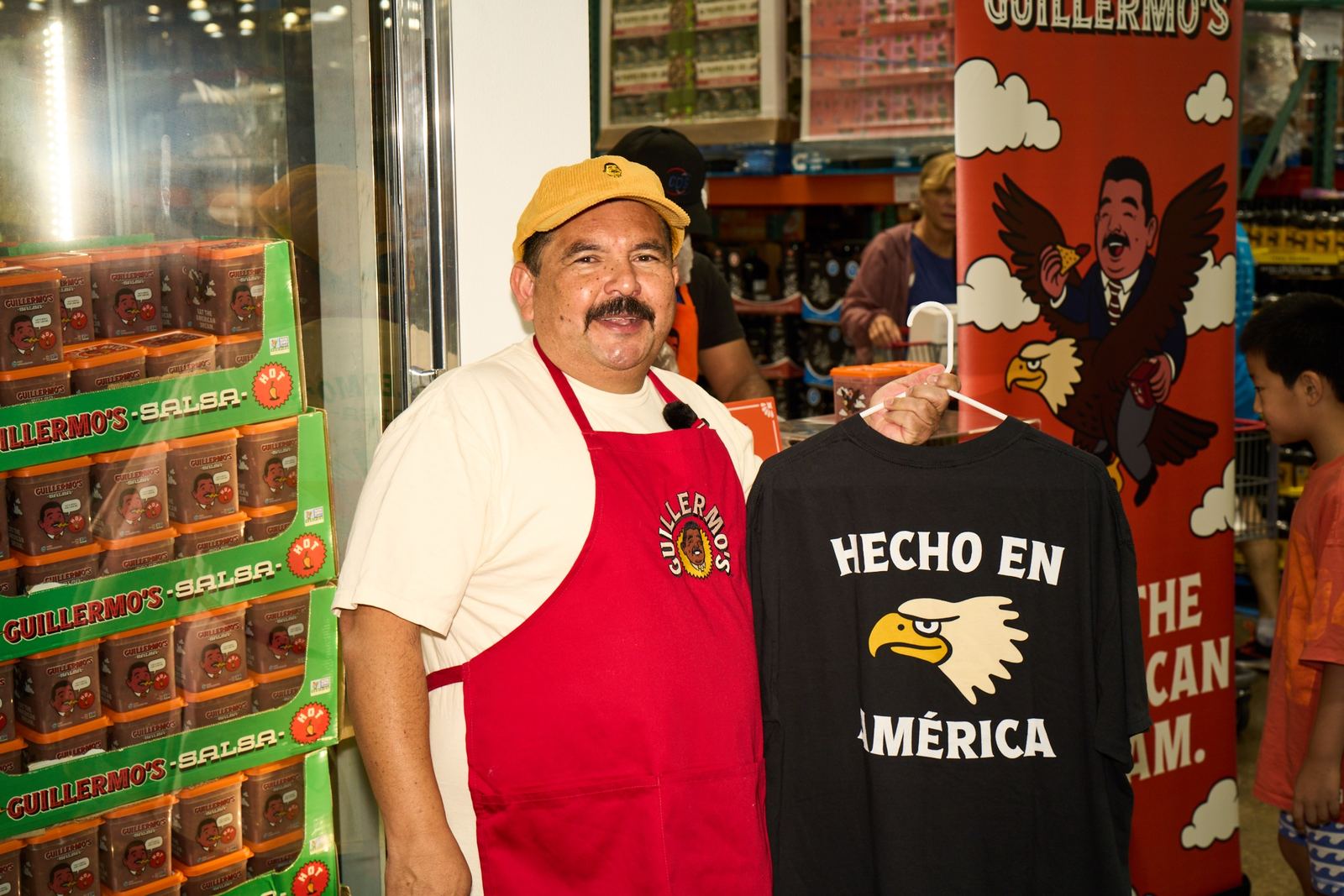 Guillermo in a Corduroy Padre Hat holding a Hecho en América tee