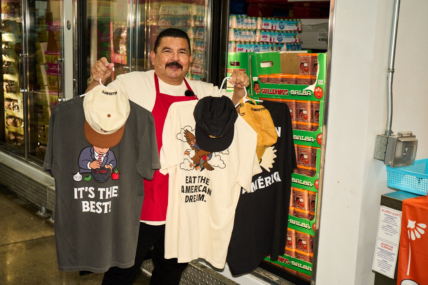 Guillermo holding three Guillermerch tees in the salsa aisle