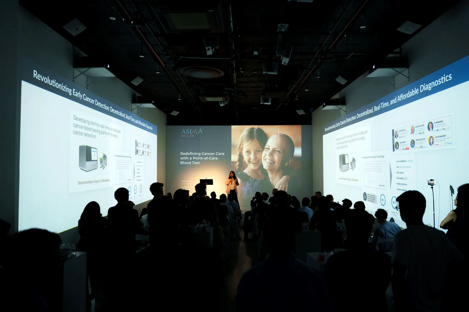 Speaker presenting to a full room with slides projected across three walls at a summit produced by LUME Studios
