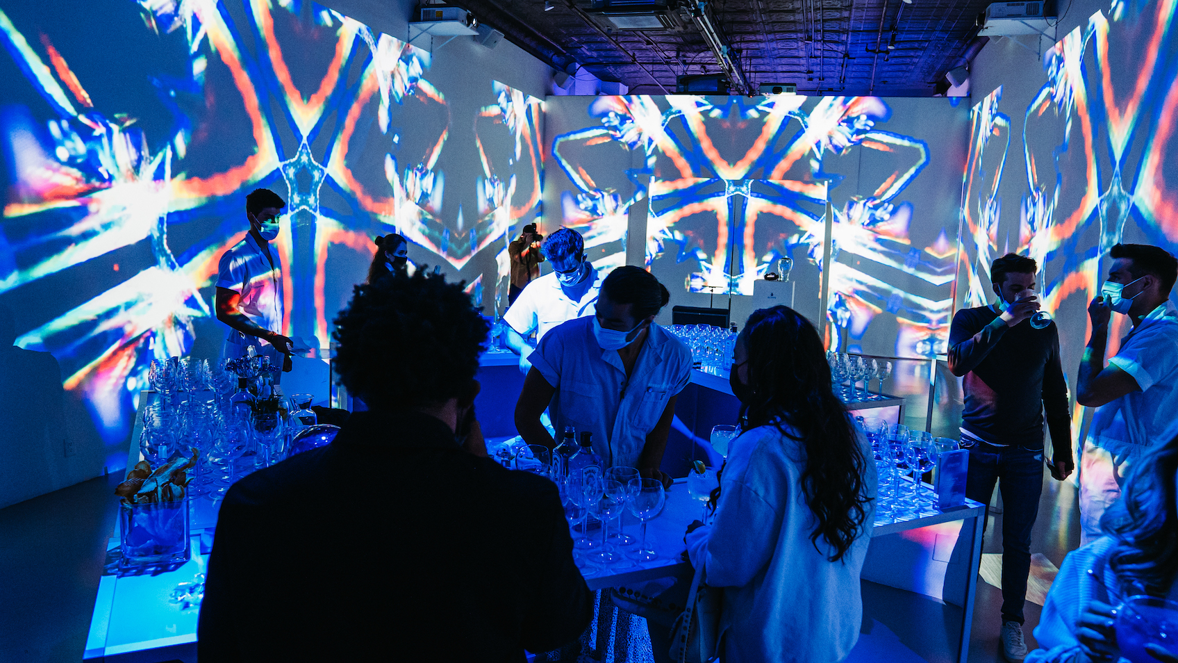 Guests gathered around cocktail tables under blue kaleidoscope projections in the Immersive Studio