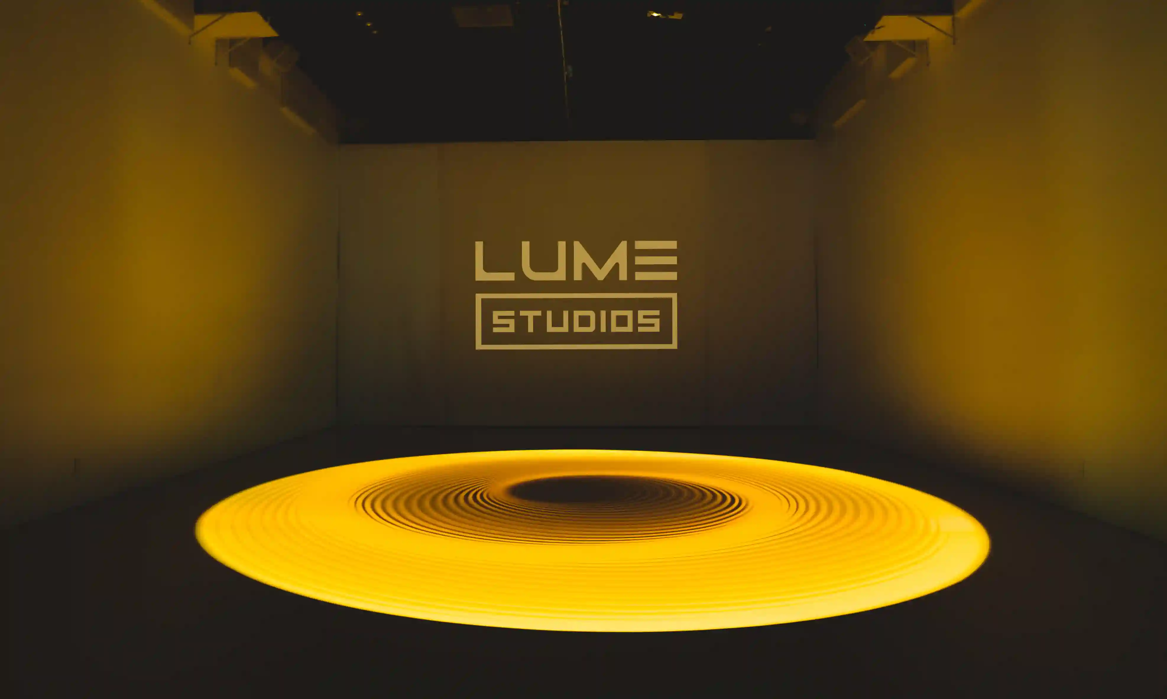 LUME Studios logo projected above a glowing yellow ring on the Immersive Studio floor