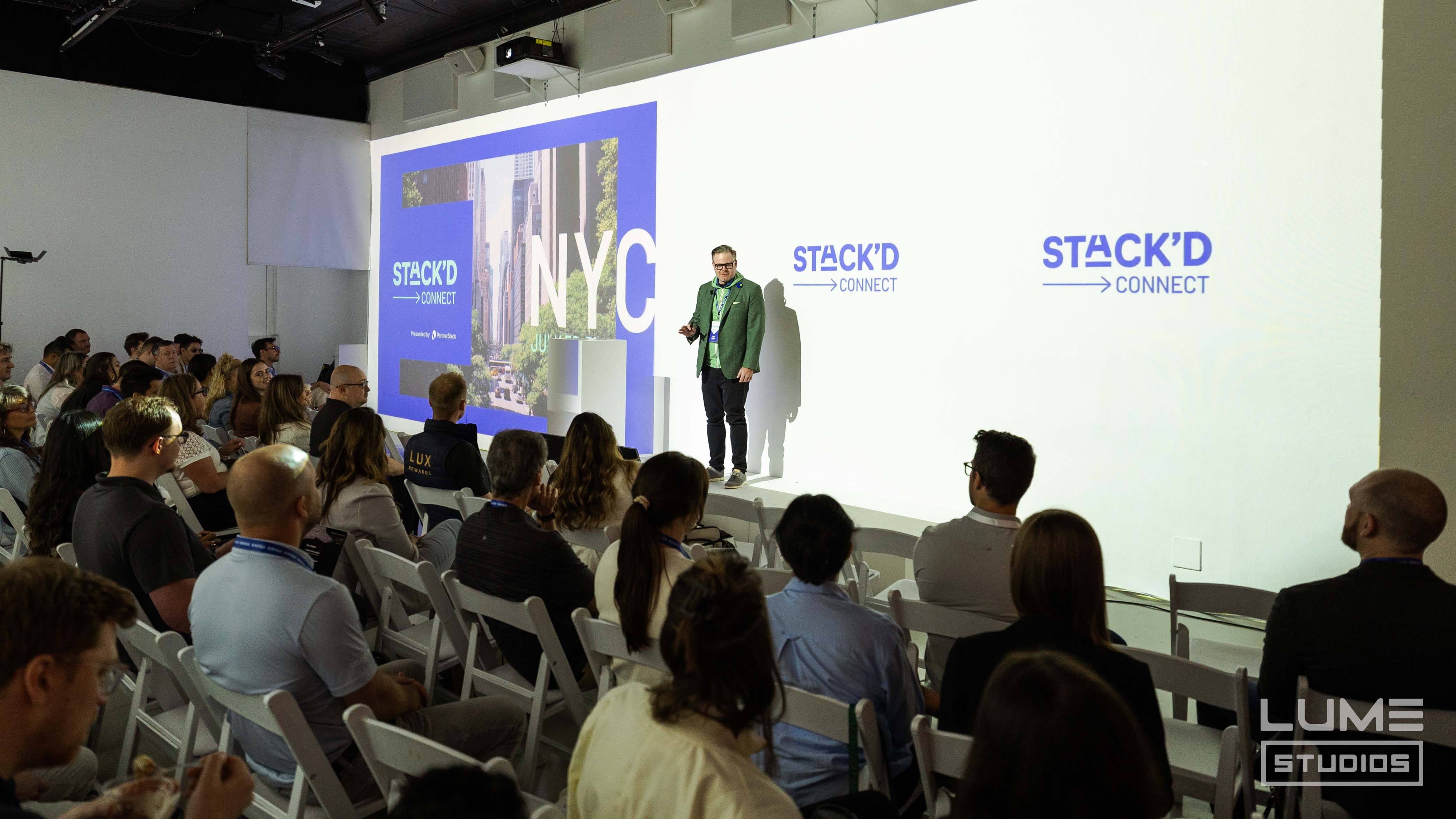 Speaker presenting to a seated audience under projected graphics at a conference produced by LUME Studios