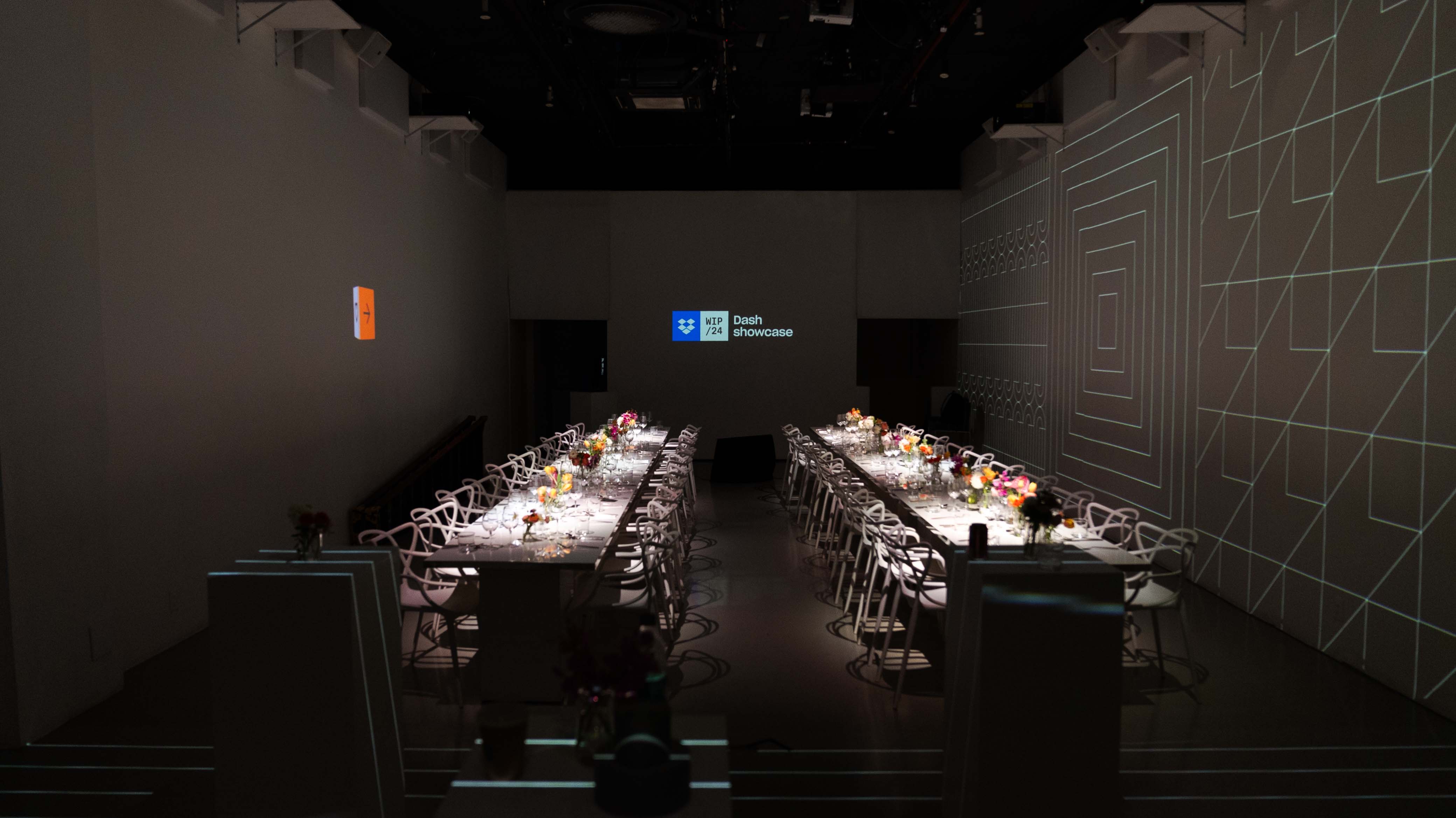 Long dinner tables set beneath a Dropbox logo and geometric wall projections in the Immersive Studio