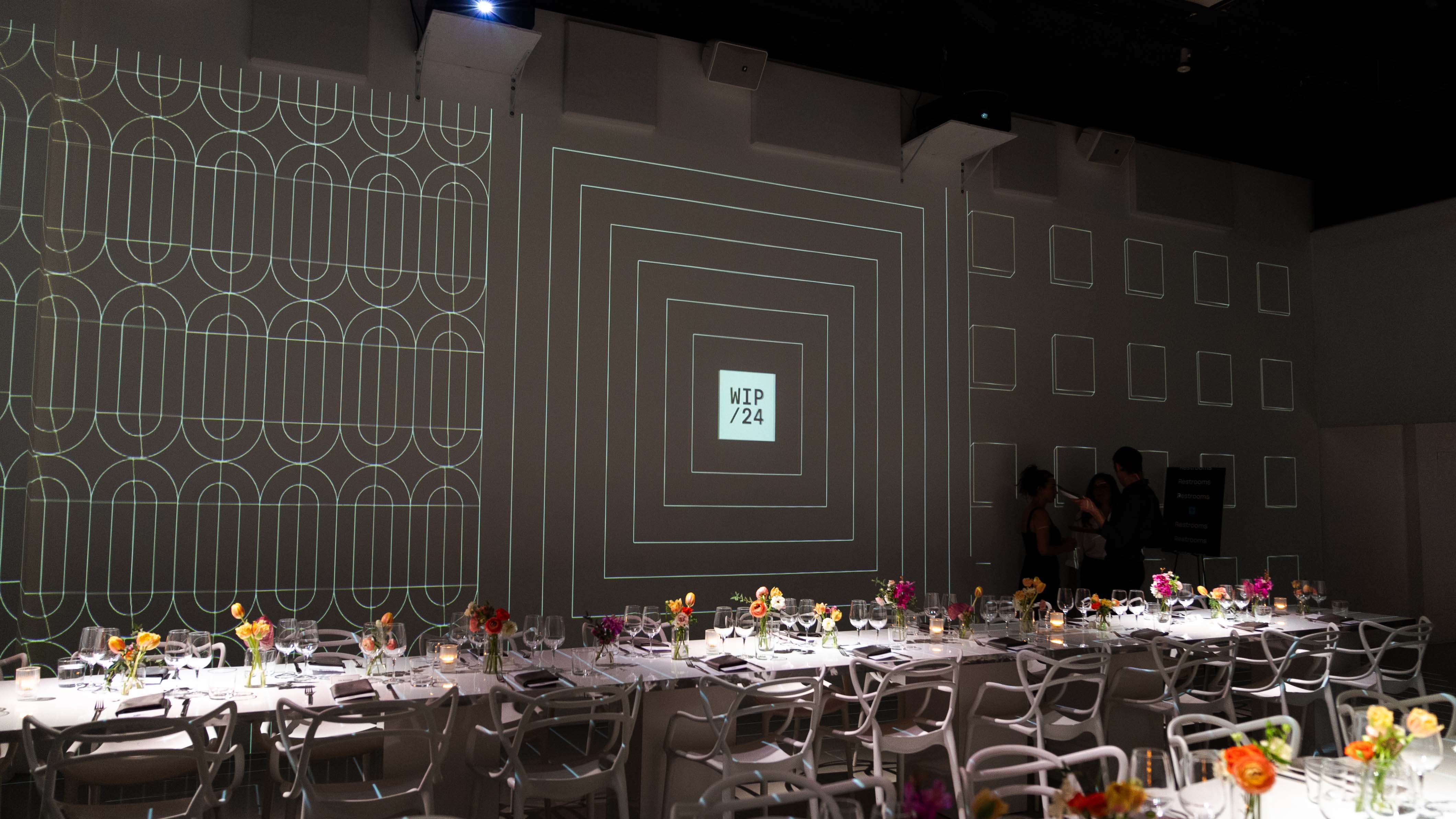 Dinner tables with flowers under geometric WIP/24 projections at the Dropbox event at LUME Studios