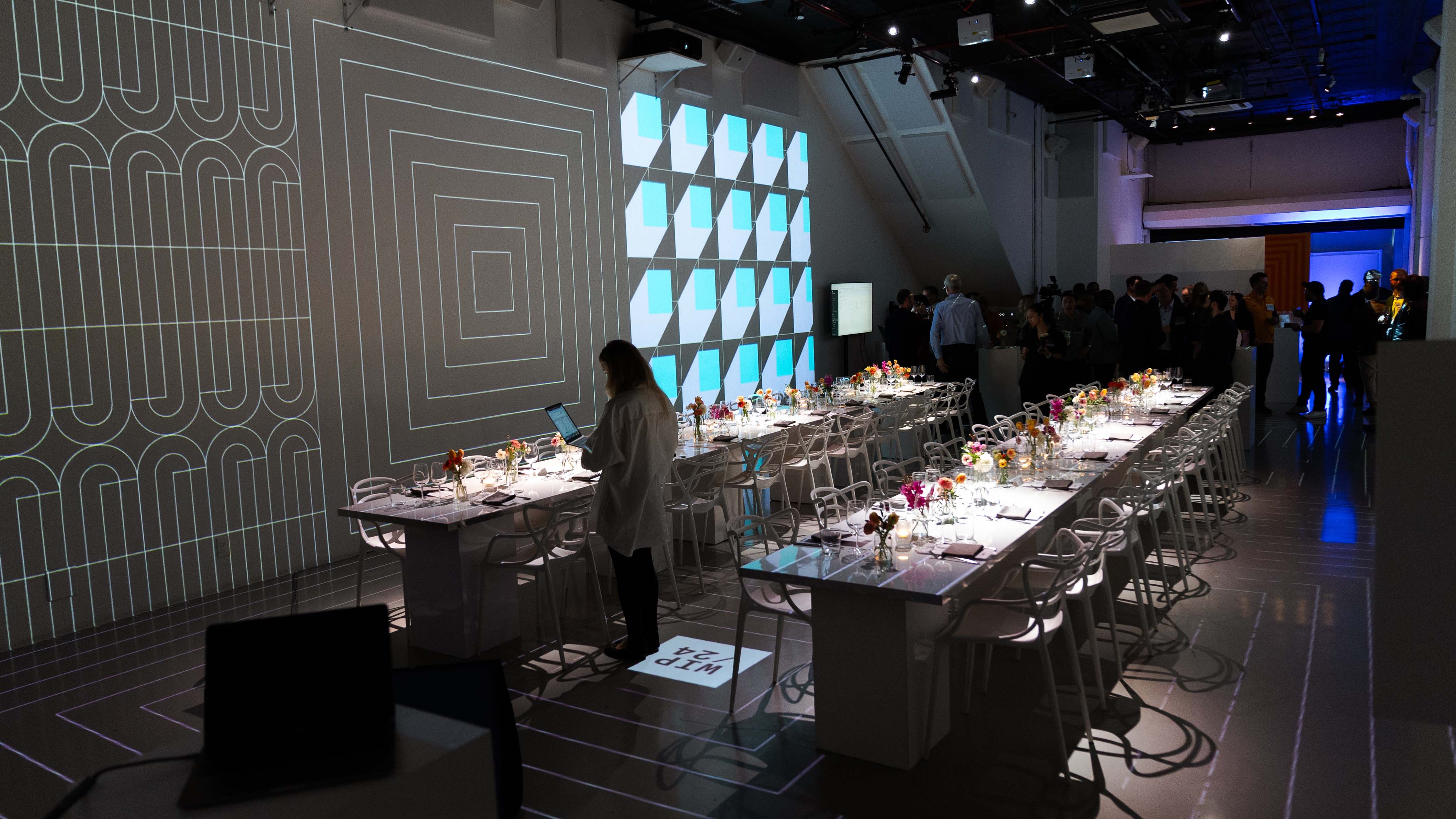Long dinner tables set beneath geometric line projections at the Dropbox dinner at LUME Studios