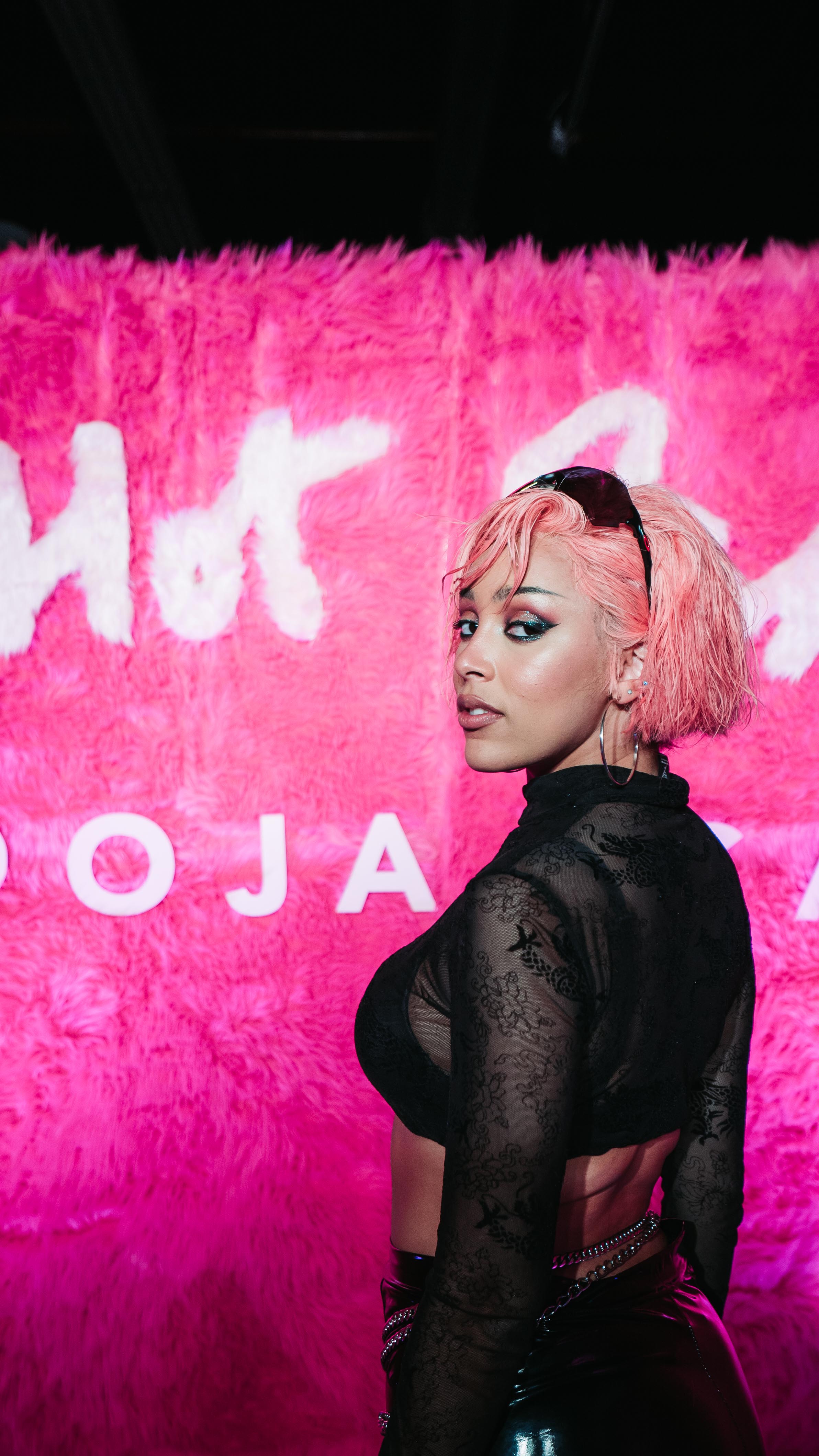 Doja Cat posing in black lace in front of the pink fur Hot Pink backdrop