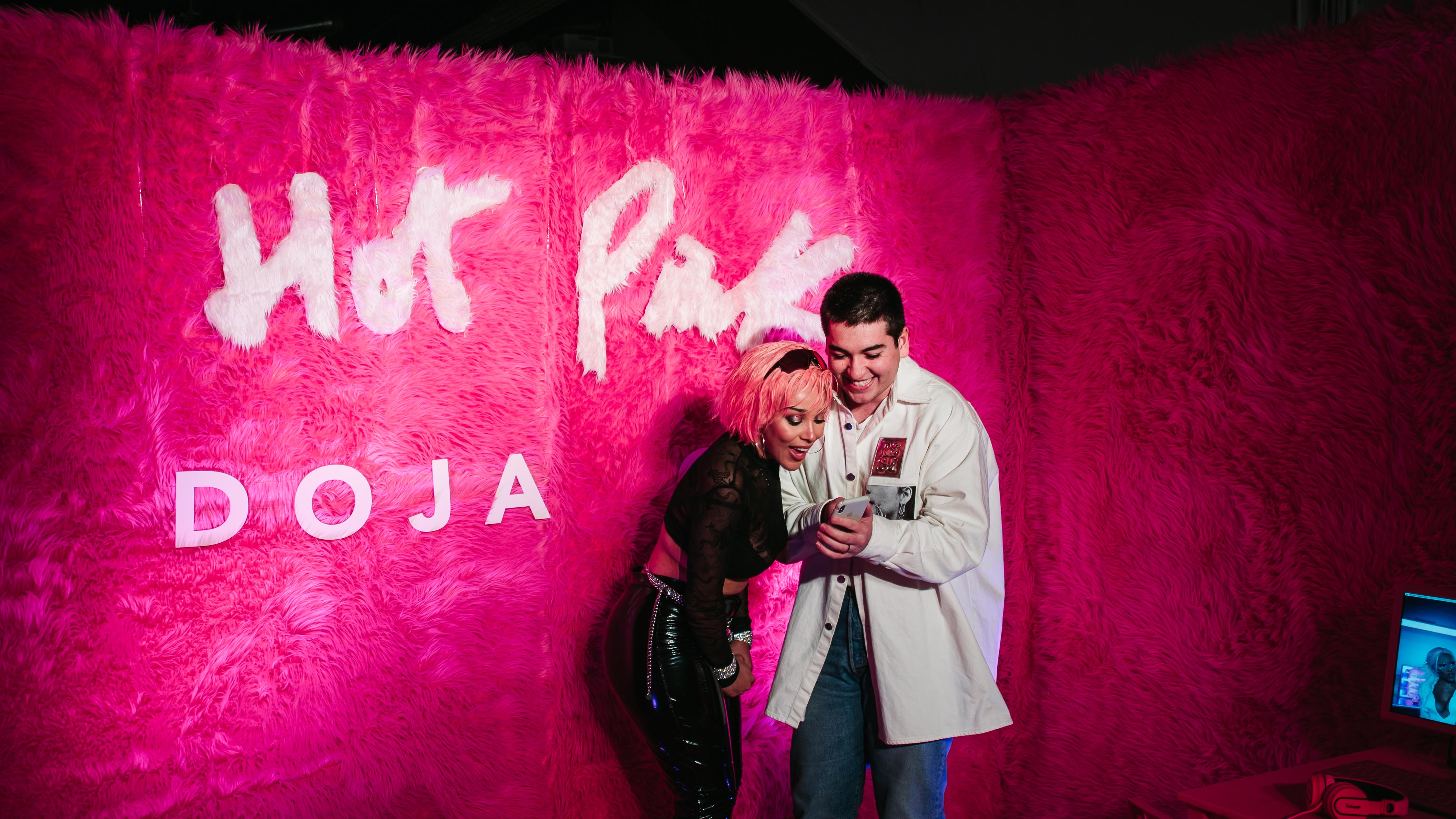Doja Cat laughing with a guest in front of the pink fur Hot Pink backdrop at LUME Studios