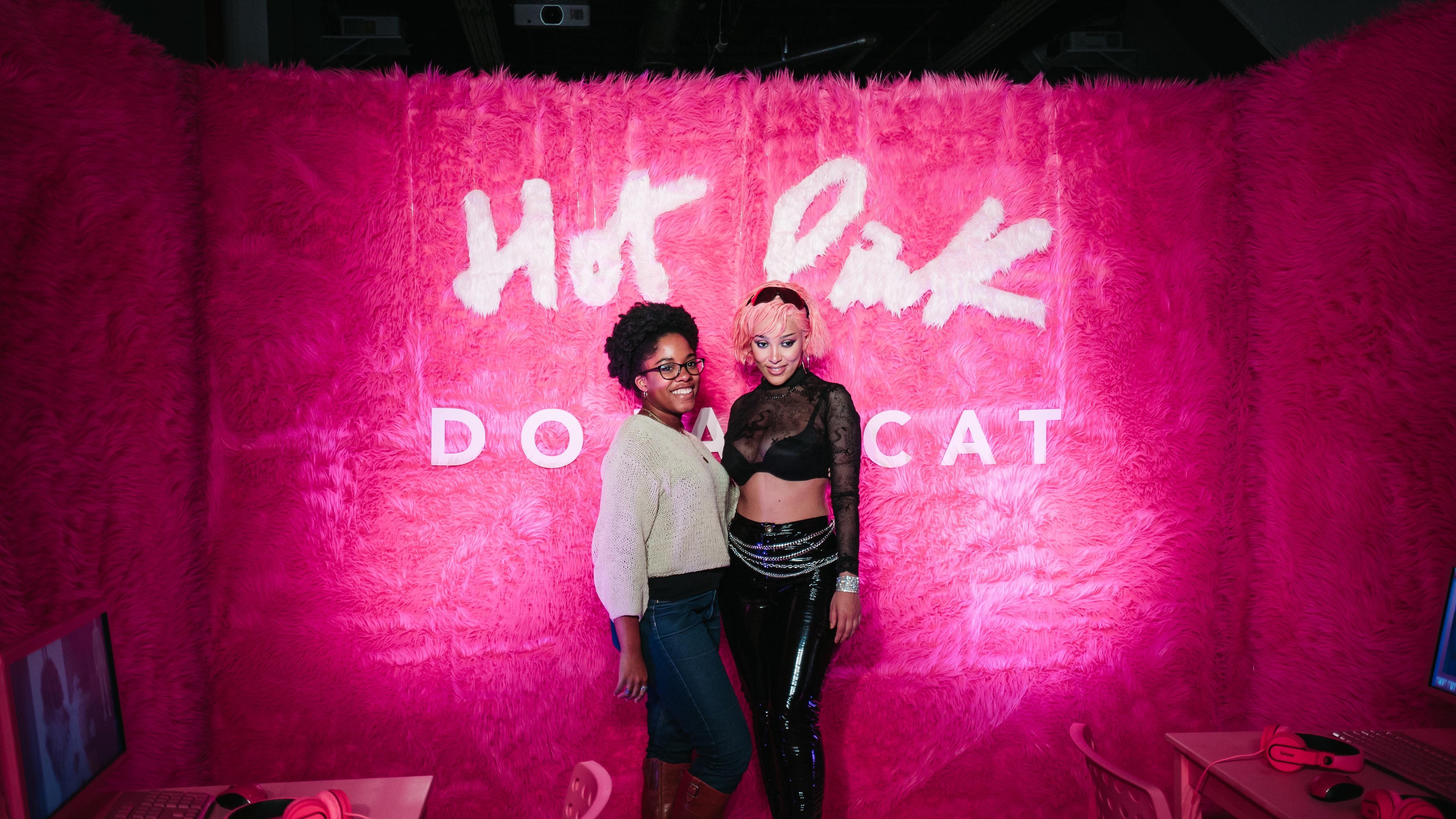 Doja Cat posing with a fan in front of the Hot Pink fur wall at LUME Studios