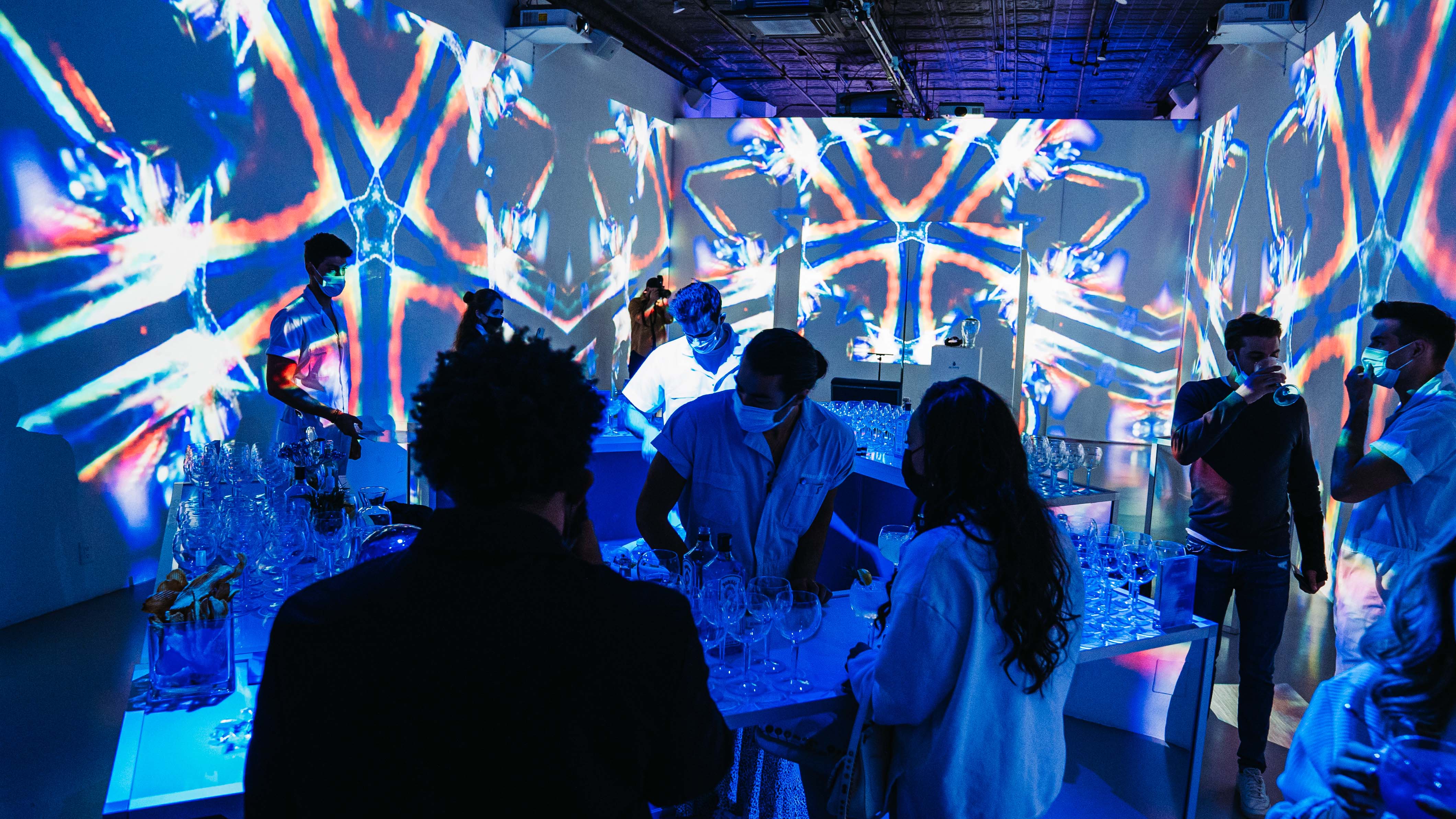 Guests at a cocktail bar under blue kaleidoscopic projections at the Bombay Sapphire x Dan Lam event
