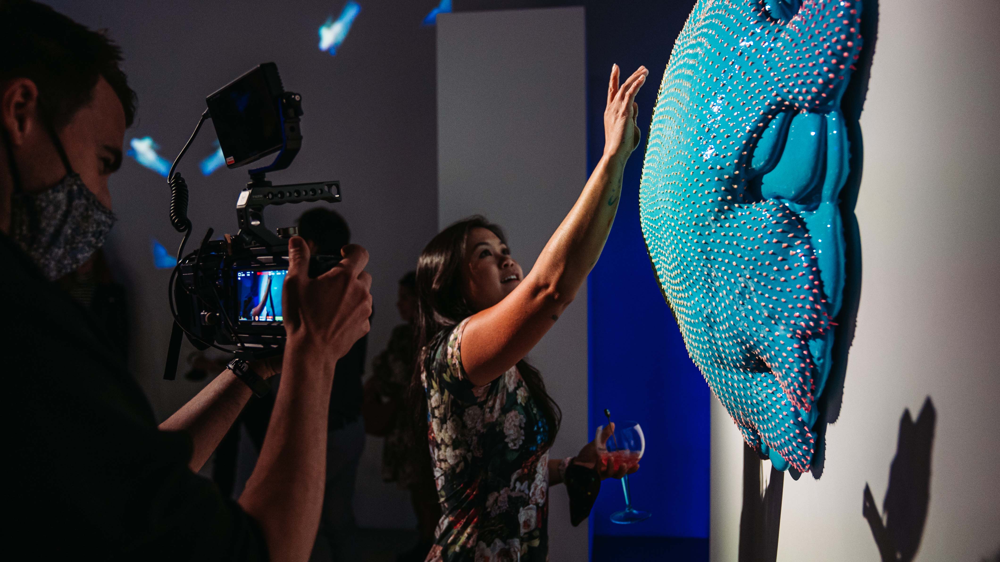 Camera crew filming a guest reaching toward a blue Dan Lam sculpture