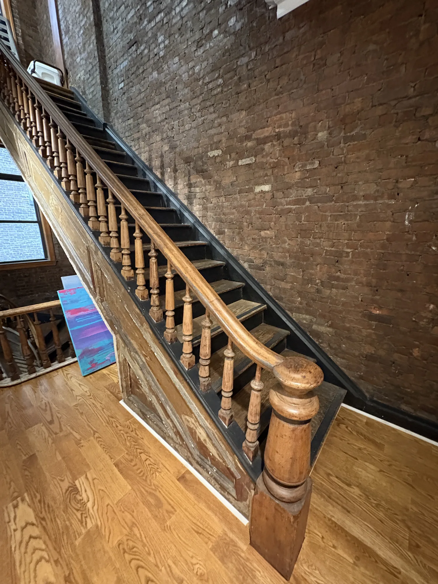 Original wood staircase with turned balusters and newel post against exposed brick wall at LUME Studios, 393 Broadway, NYC film location