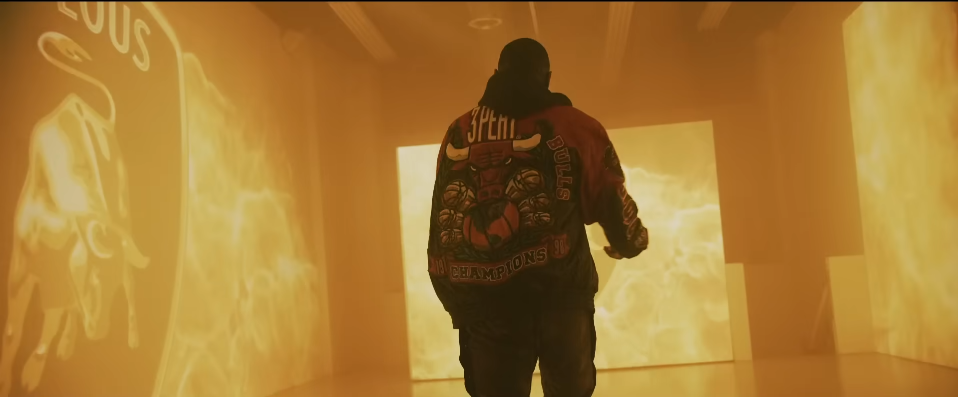 Performer in a Chicago Bulls jacket walks through a room of fiery projections on the Fabolous B.O.M.B.S. video set.