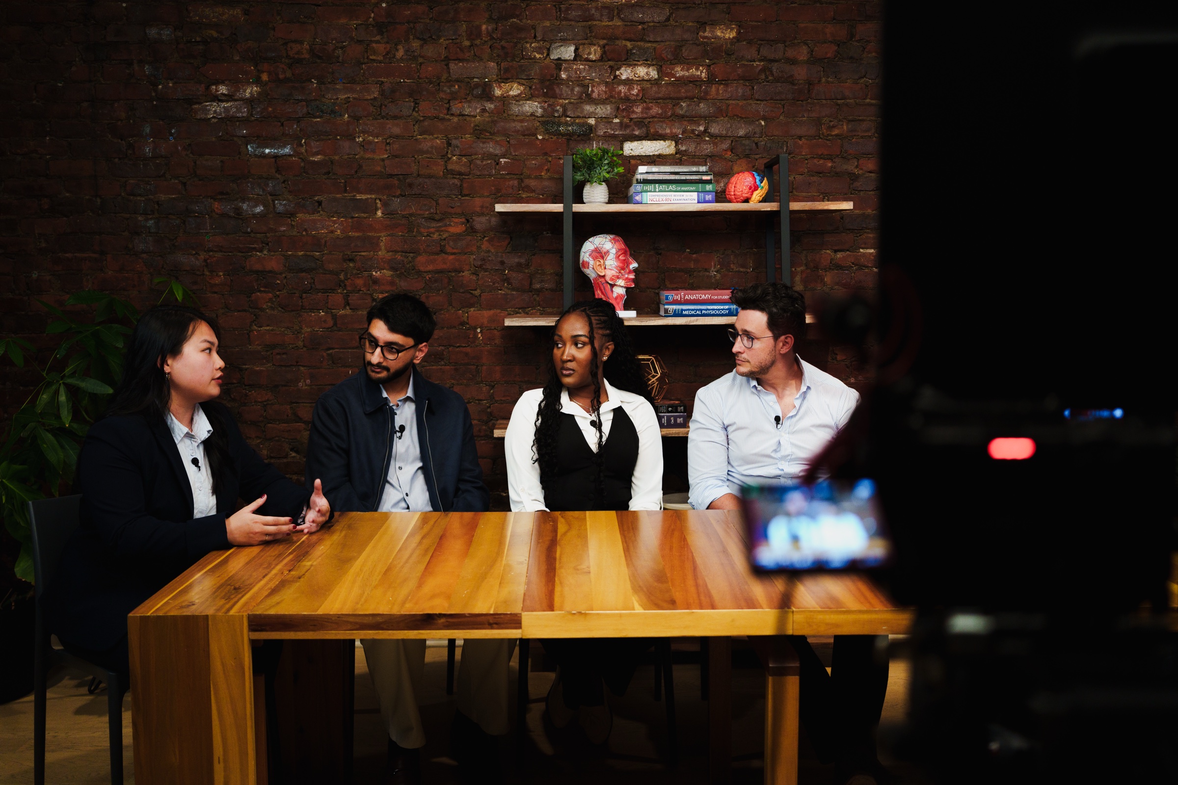 Doctor Mike and students mid conversation at the table with a camera screen glowing in the foreground.