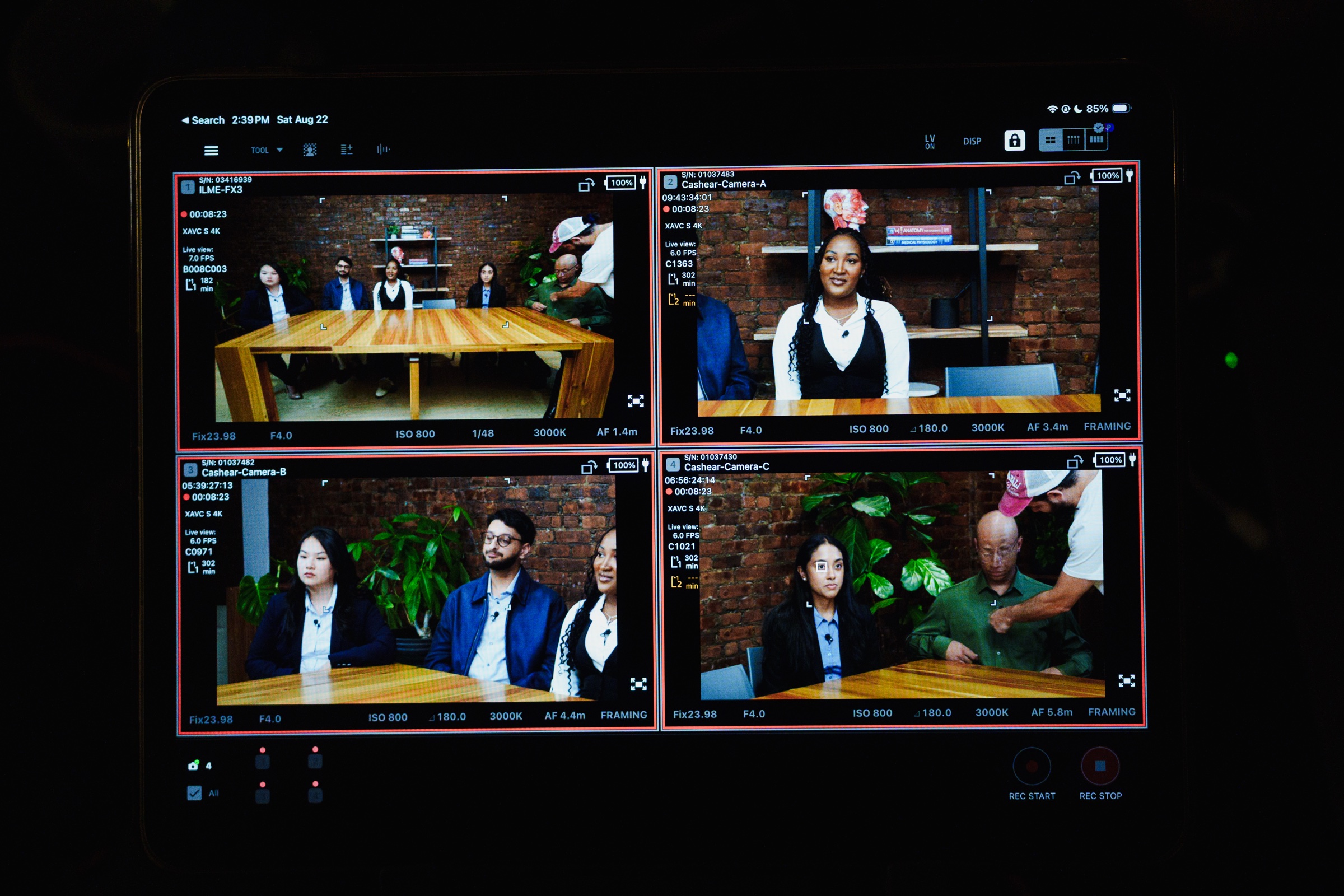 A monitor split into four synced camera feeds of the podcast table from different angles.