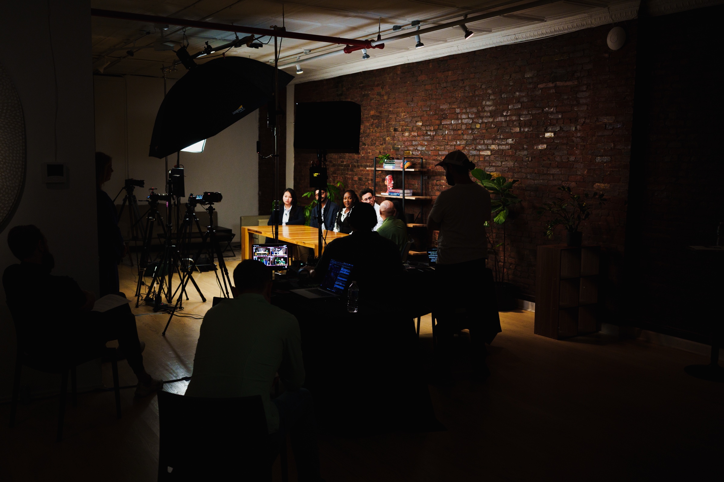 Wide view of LOFT 4 darkened for the shoot, the lit podcast table at the far end and crew watching monitors.