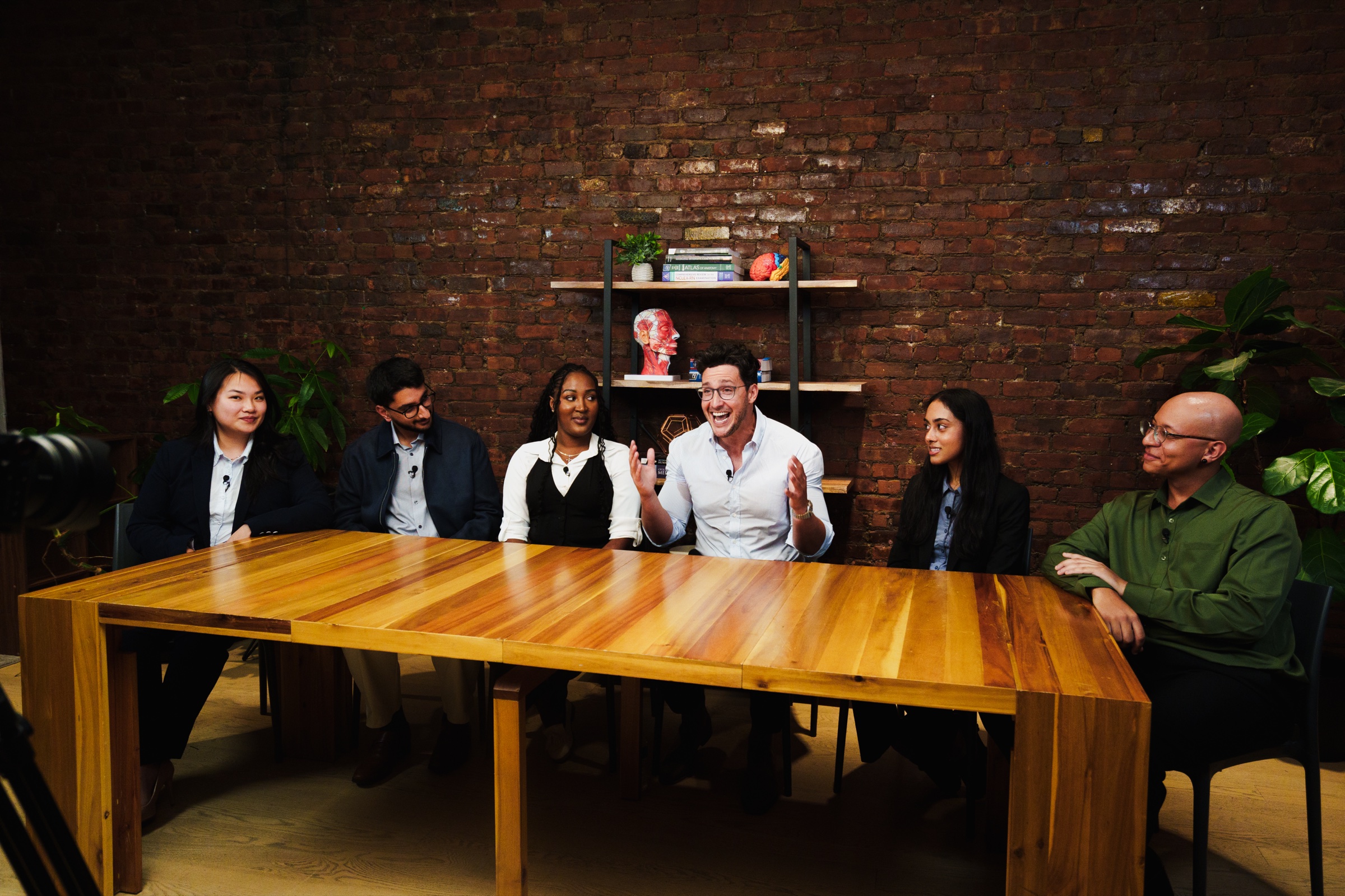 Doctor Mike speaks with his hands raised as the students laugh along the table during the Elsevier podcast shoot.