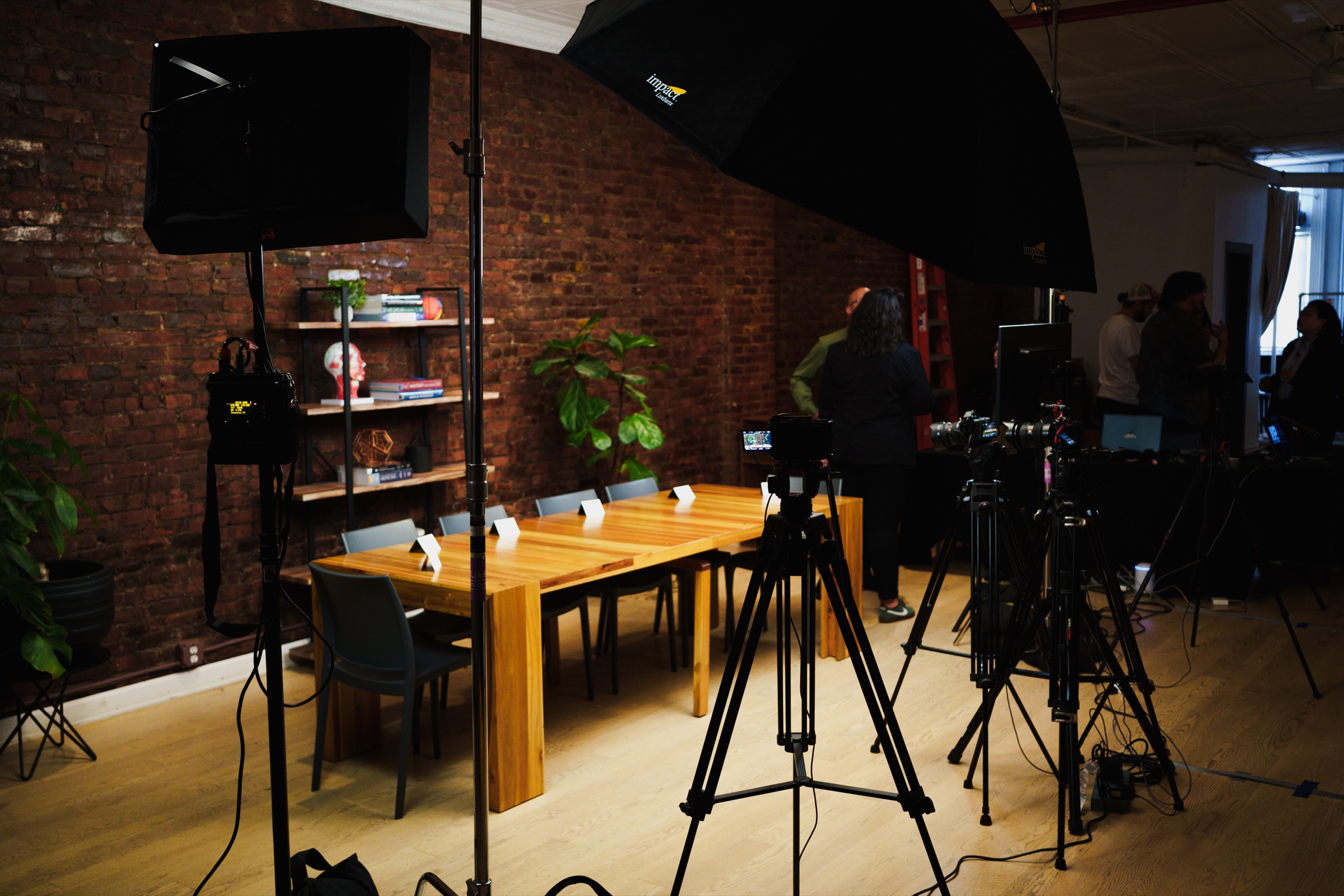 The podcast set in LOFT 4 before taping, a long wooden table lit warm against brick with cameras in place.