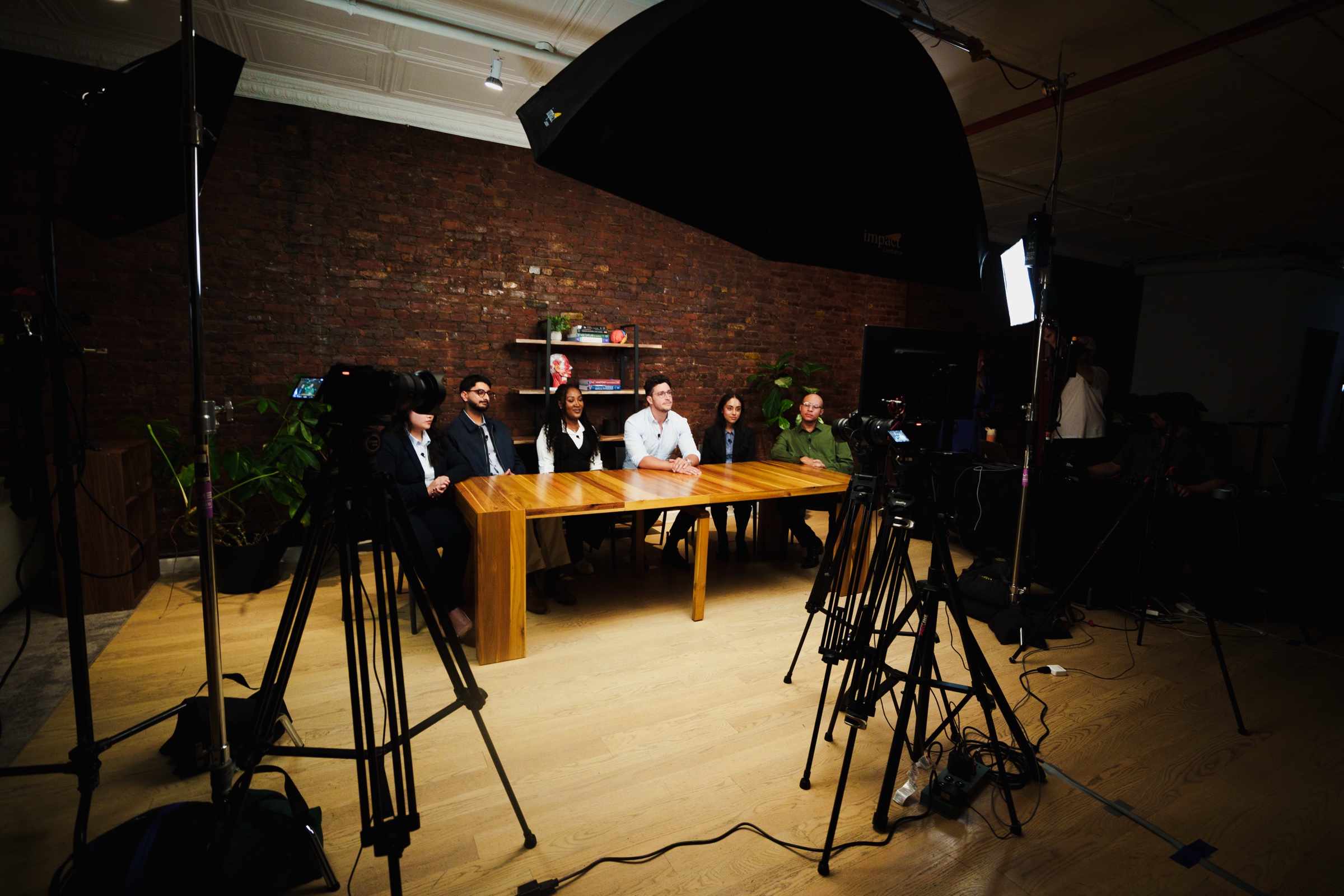 Two cameras on tripods face the table where Doctor Mike and the students sit under an umbrella light.