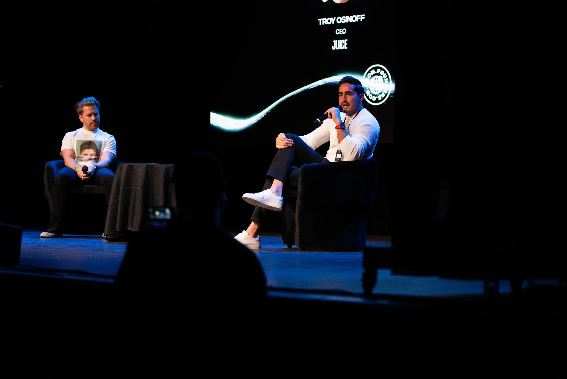 Comfrt fireside chat on stage at the Q4 Summit, lit against the dark LED wall.