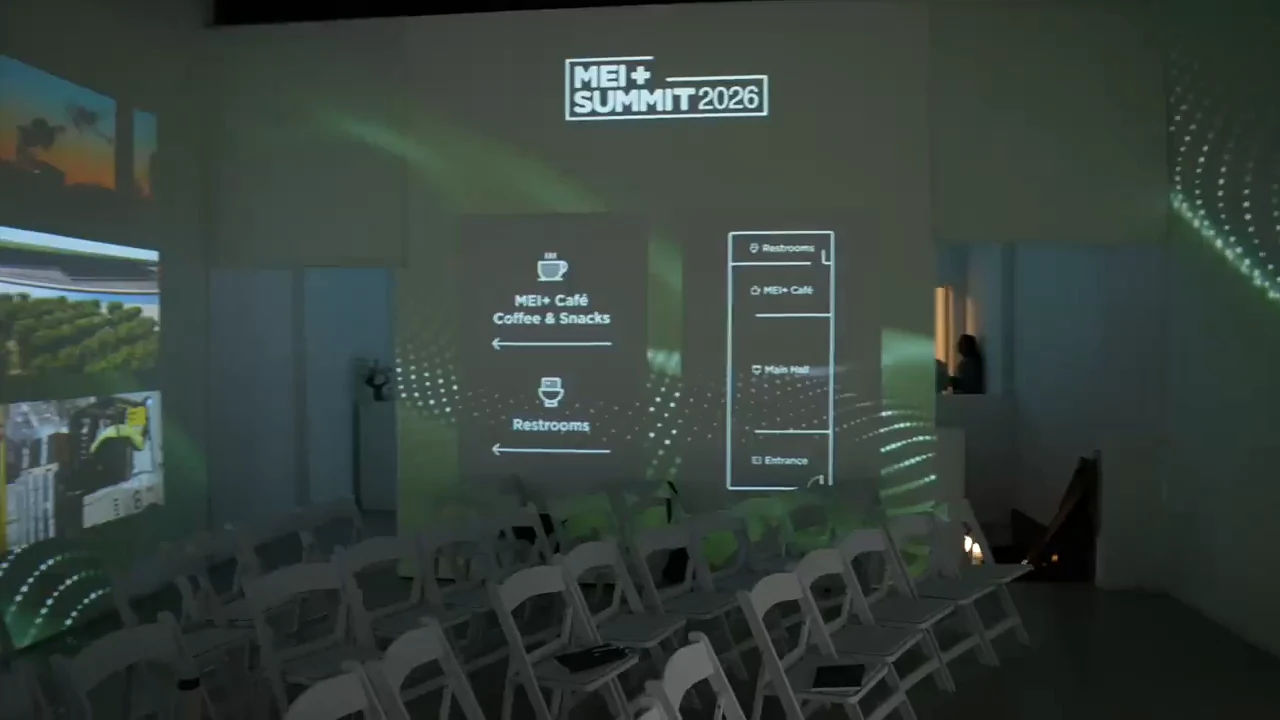 The Immersive Studio set with rows of white chairs before doors, with projected wayfinding to the MEI+ Café and the restrooms.
