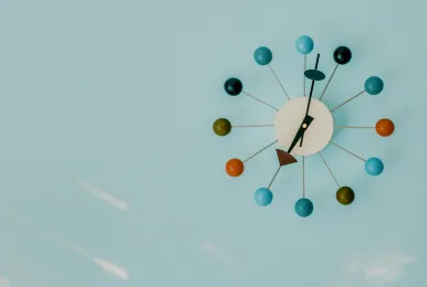 Modern wall clock with colorful round markers on a light blue wall.