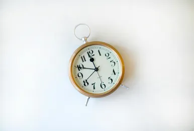 Vintage round wall clock with black numbers and hands showing time 10:55 on a white background.