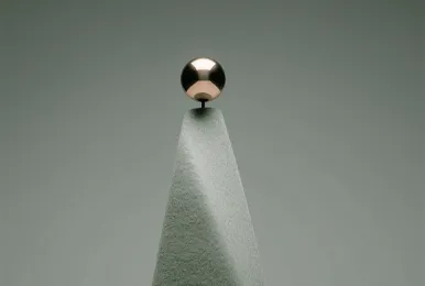 Minimalist sculpture with a smooth triangular stone base topped by a reflective metallic sphere.