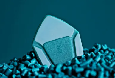 Close-up of a light blue polymer pellet among smaller cylindrical blue plastic pellets.