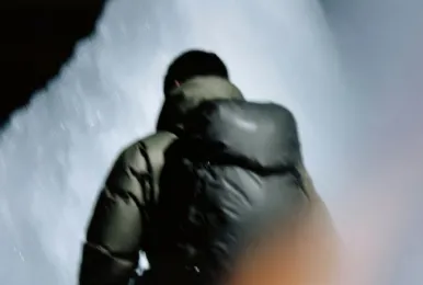 Person wearing a dark puffer jacket standing in front of a waterfall at night.