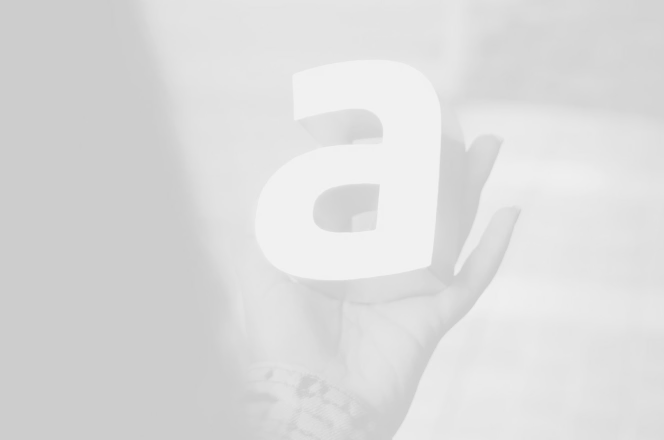 Close-up of a hand holding a 3D lowercase letter 'a' in grayscale.