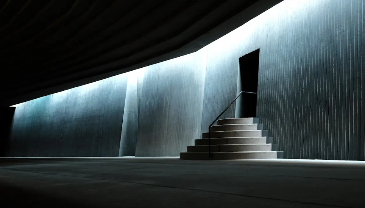 Dimly lit modern interior with stepped circular platform leading to a dark doorway against a ribbed wall.