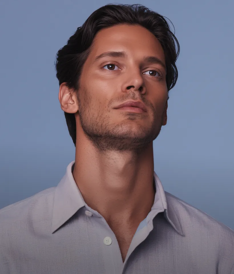 Portrait of a man with dark hair wearing a light gray shirt against a plain blue background.