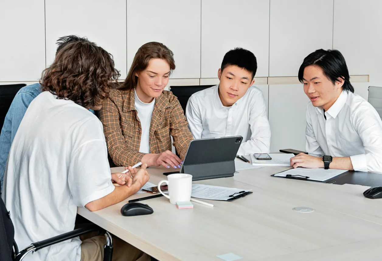 Four young professionals sitting around a conference table collaborating and looking at a tablet.