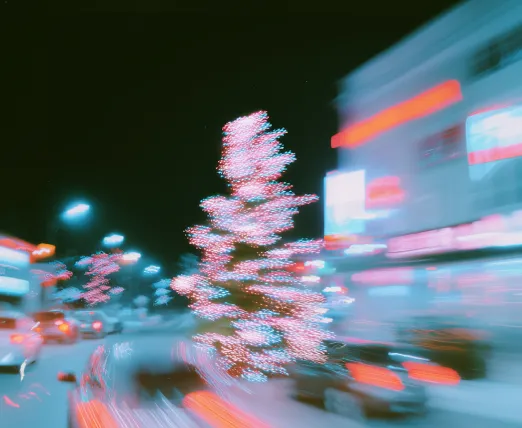 Blurred image of a Christmas tree decorated with lights on a busy city street at night.