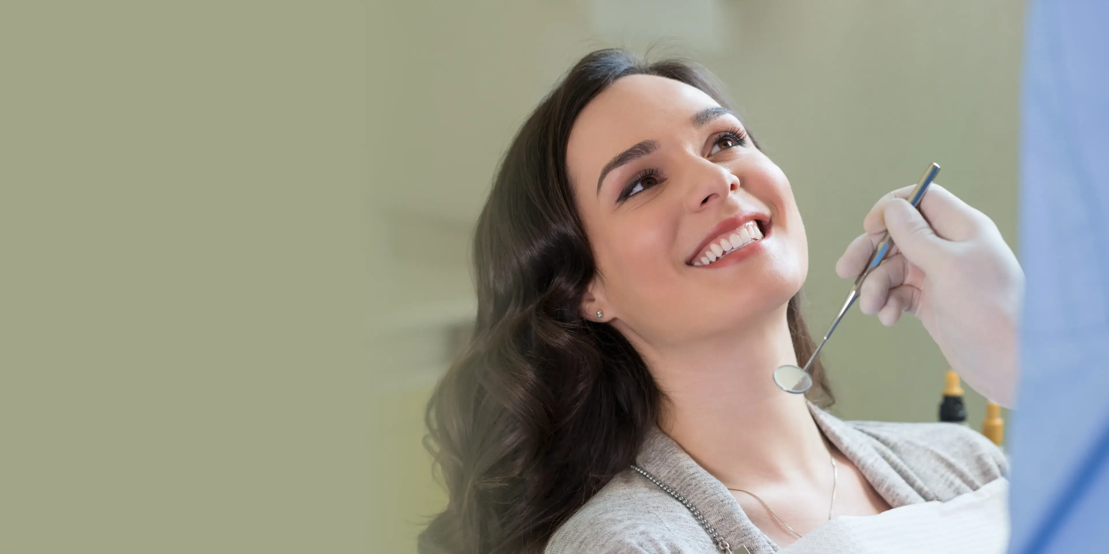Smiling woman reclined in dental chair with dentist holding a dental mirror near her mouth.