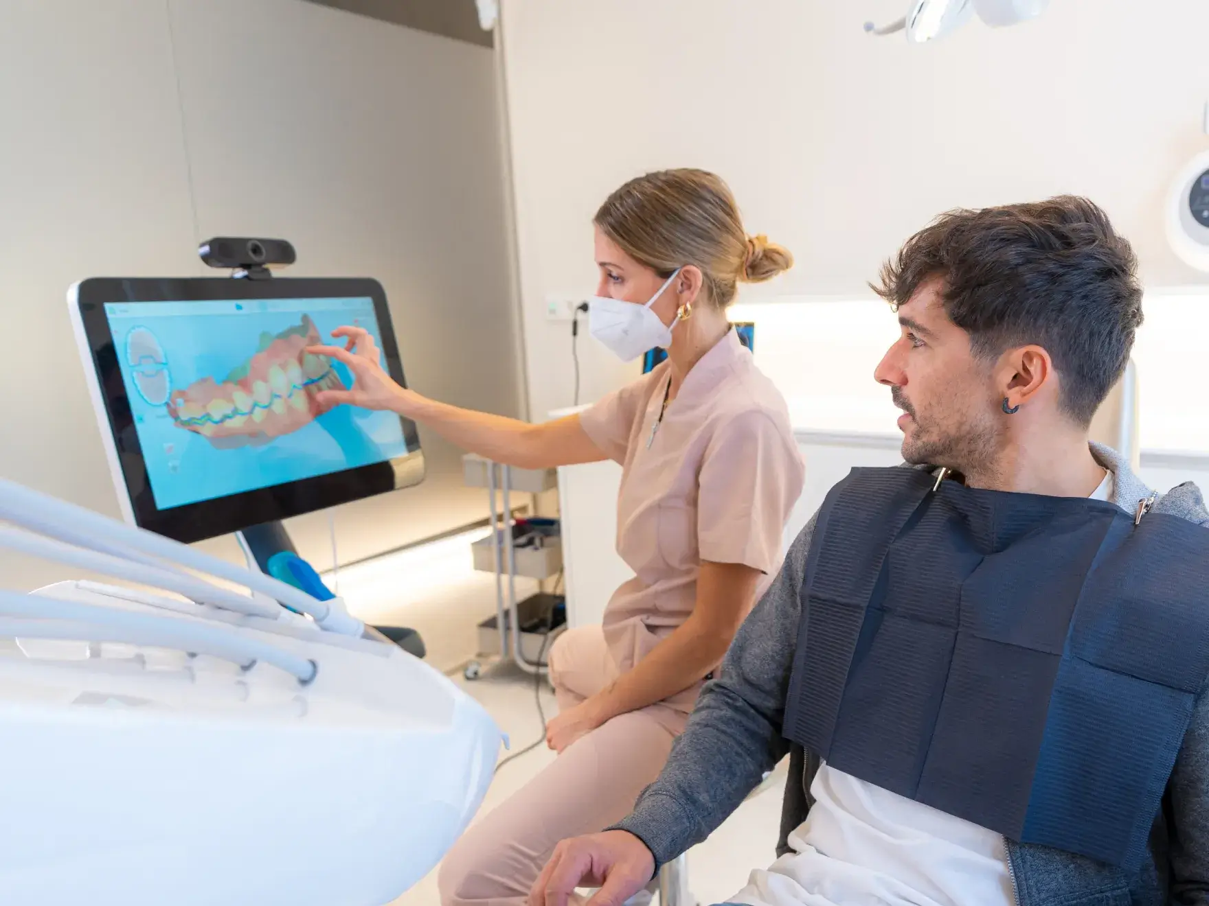 Dentist wearing a face mask showing a 3D digital dental scan to a male patient seated in a dental chair.