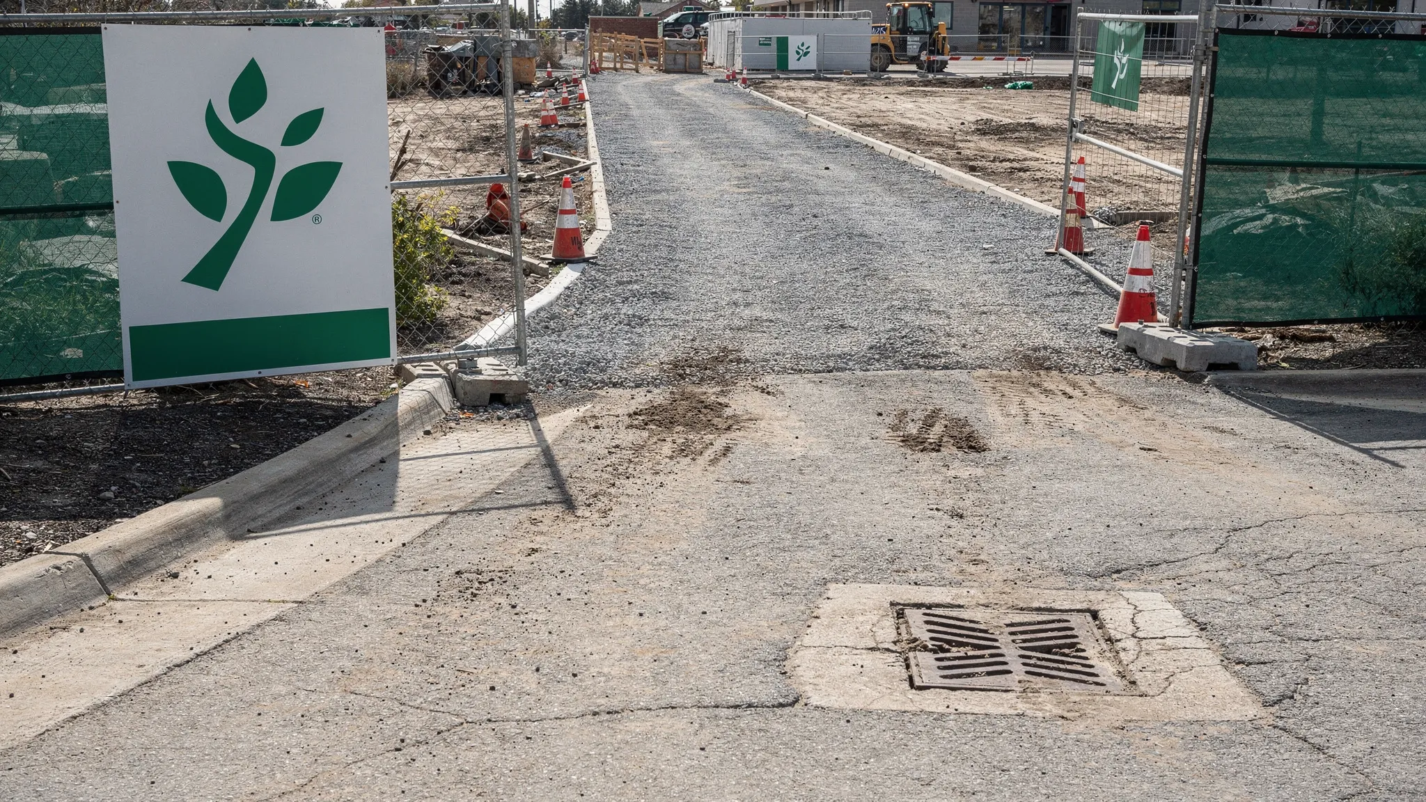 A clean commercial jobsite entrance with a swept curb line, clear gutter, visible storm drain inlet free of sediment, and a construction access drive free of track-out.