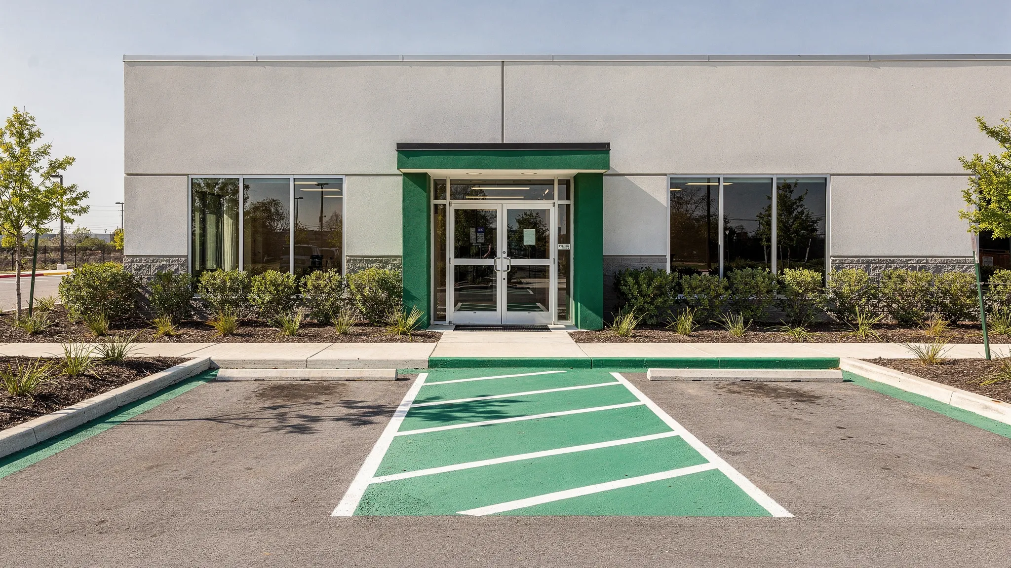 A clean commercial property exterior with swept parking spaces, clear curb lines, open drive lanes, a visible building entrance, and tidy landscaped edges.