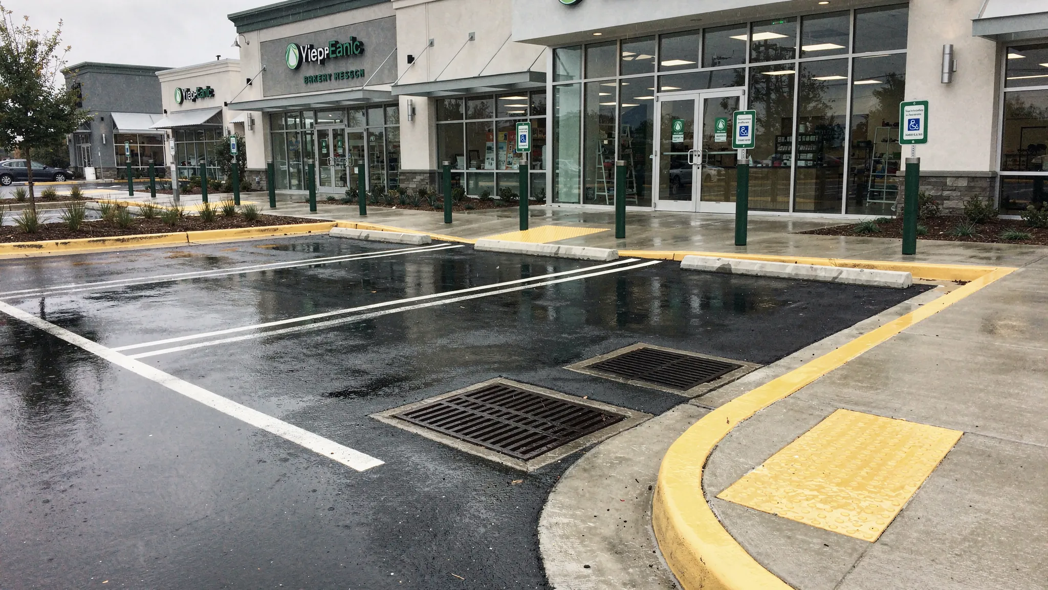 A clean commercial parking lot after rainfall with clear curb lines, visible storm drain grates, no sediment piles, and safe pedestrian paths near storefront entrances.