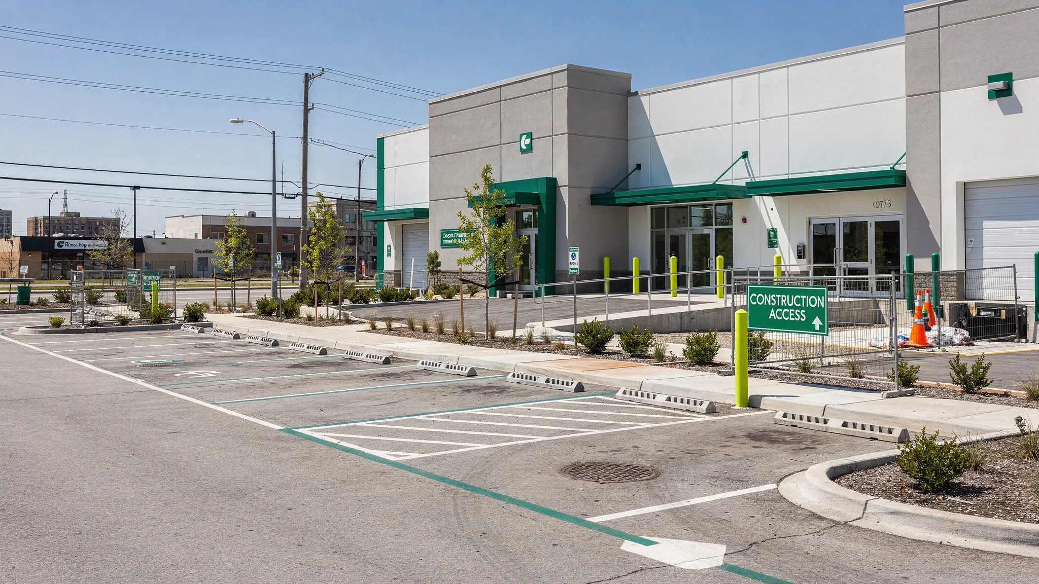 A clean commercial property exterior along a suburban-to-urban corridor, showing a swept parking lot, clear curb lines, open storm drain inlets, tidy entrances, a loading dock, and a marked construction access point.