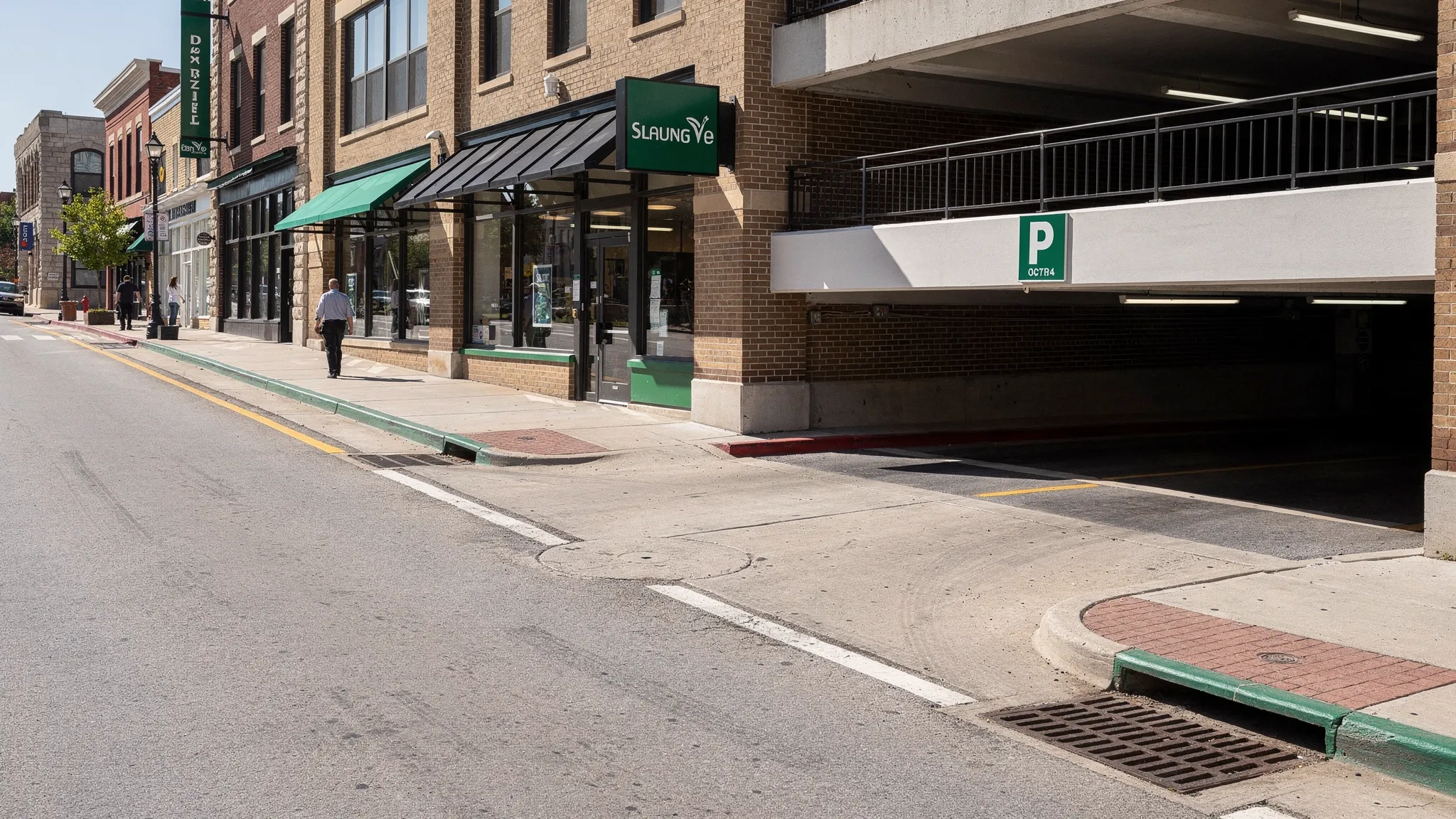 A clean downtown Nashville street edge with storefronts, parking garage entrances, curb lines, storm drain inlets, and light pedestrian activity, showing the types of exterior zones that need coordinated cleanup.
