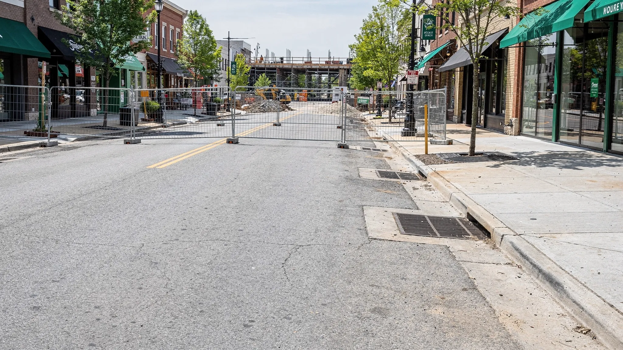 A clean Nashville commercial street after sweeping with clear curb lines, open storm drain inlets, tidy sidewalks, and construction fencing set back from the roadway.