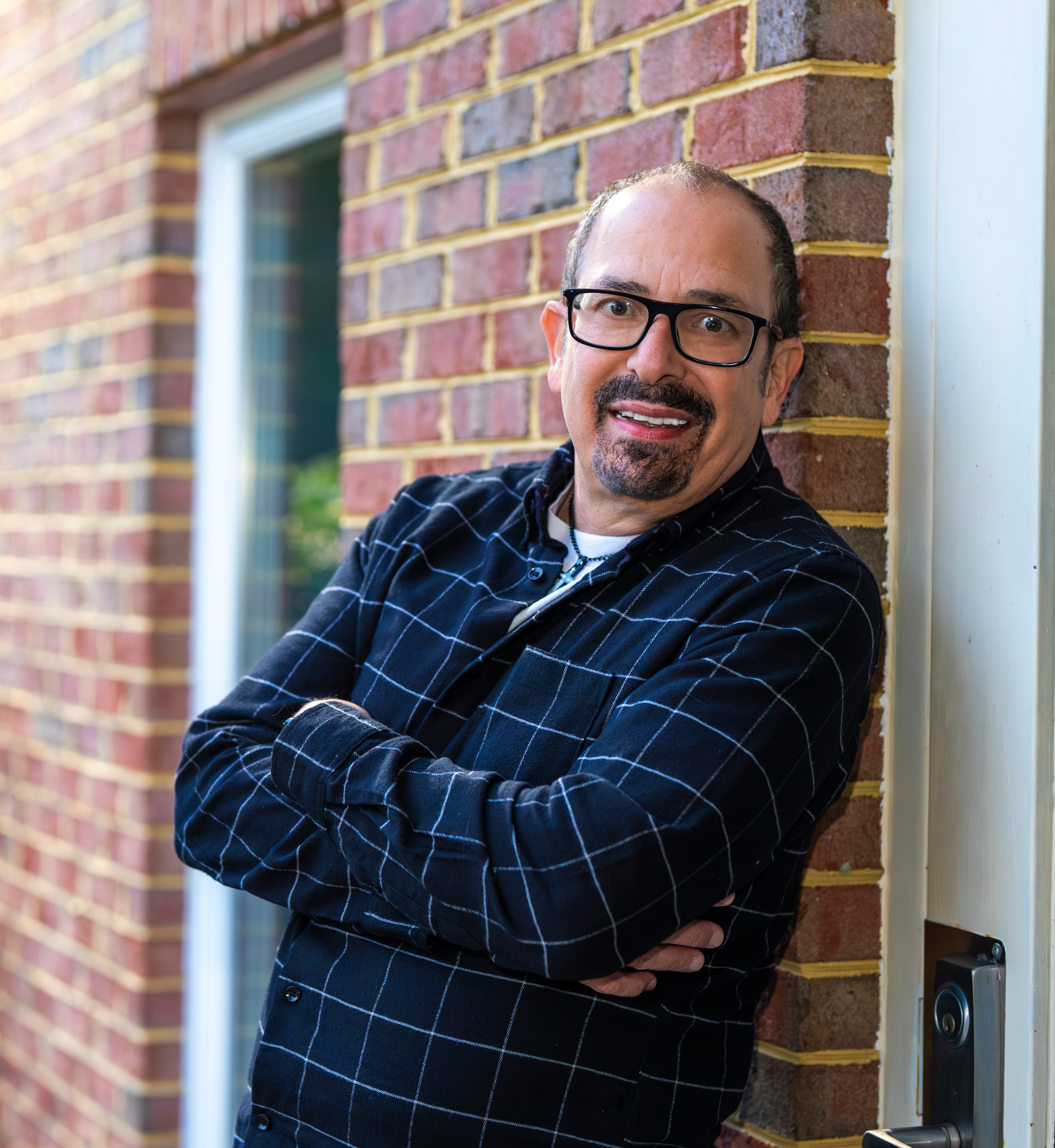 Portrait of comedian Nazareth smiling with arms crossed against a brick wall