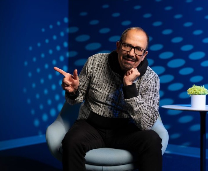 Nazareth seated on stage during a standup comedy performance under blue lights