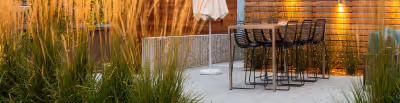 Outdoor dining area with tall grasses, a black metal table and chairs, and a white patio umbrella.