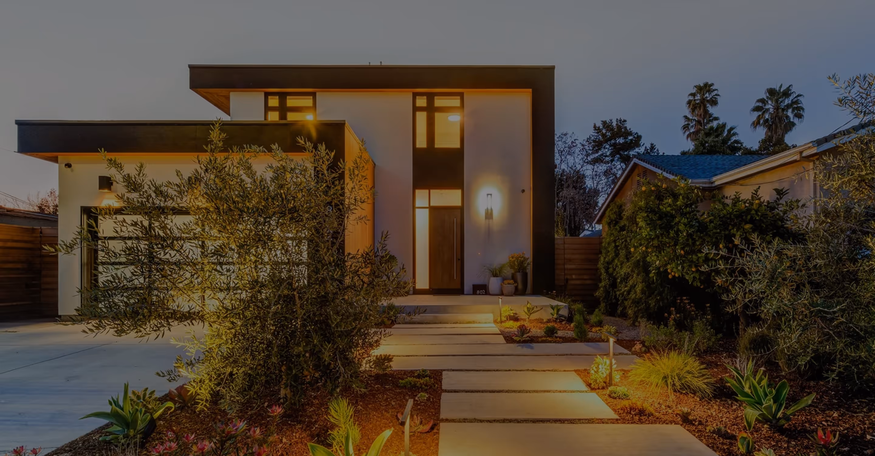 Modern two-story house with illuminated pathway and landscaped front yard at dusk.